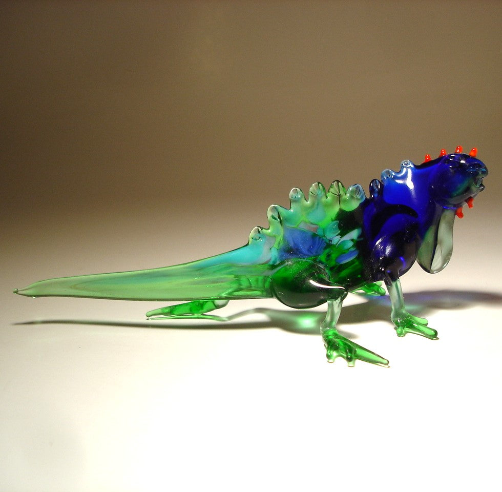 A hand-blown glass lizard figurine with a translucent blue head and neck, green body, and small red spines.