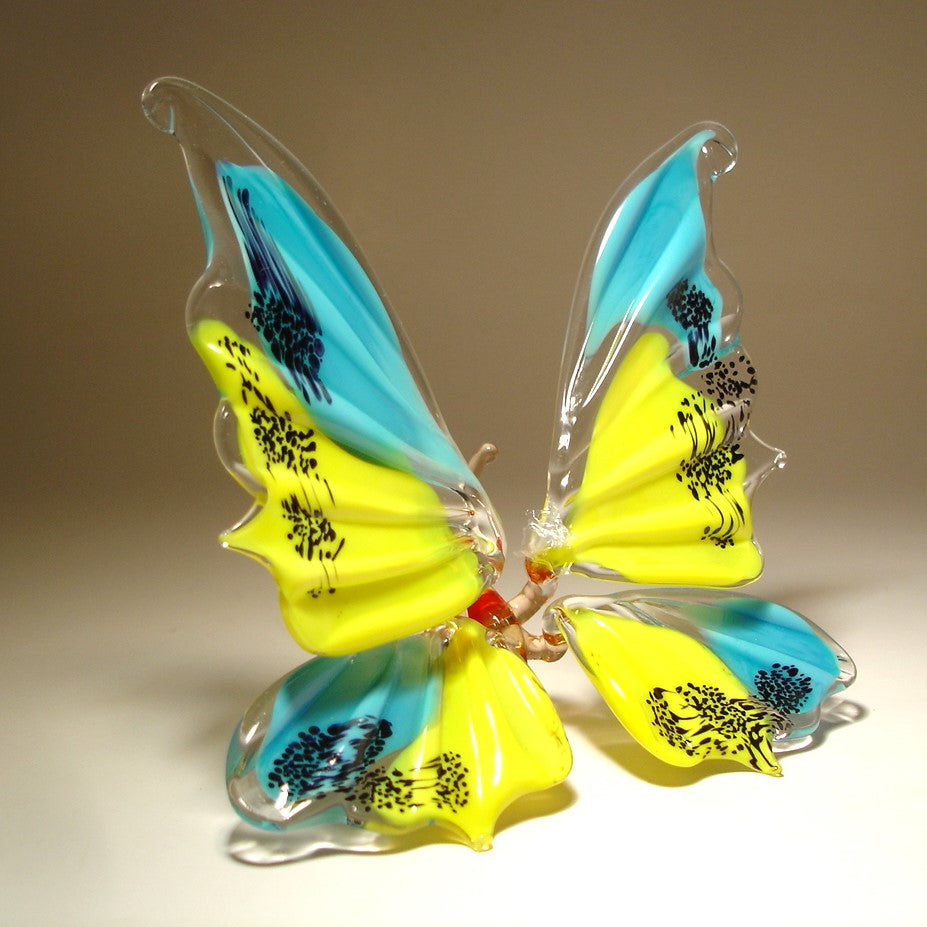 A handcrafted glass butterfly sculpture with vibrant yellow, light blue, and black painted details.