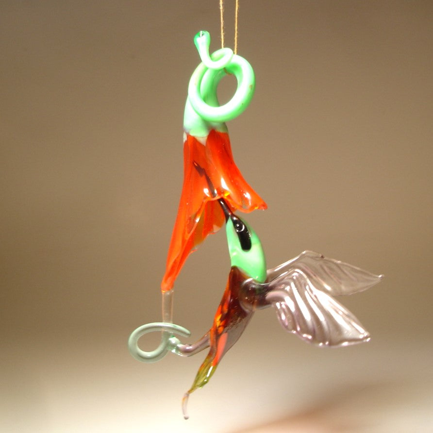 Glass hanging green and purple hummingbird ornament on a red trumpet flower.