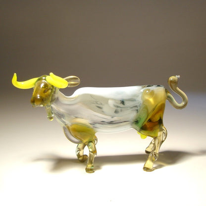 Side view of the glass cow figurine, showcasing its detailed legs, curled up tail, and white body.