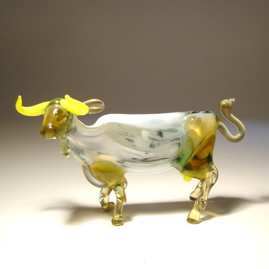 Side view of the glass cow figurine, showcasing its detailed legs, curled up tail, and white body.