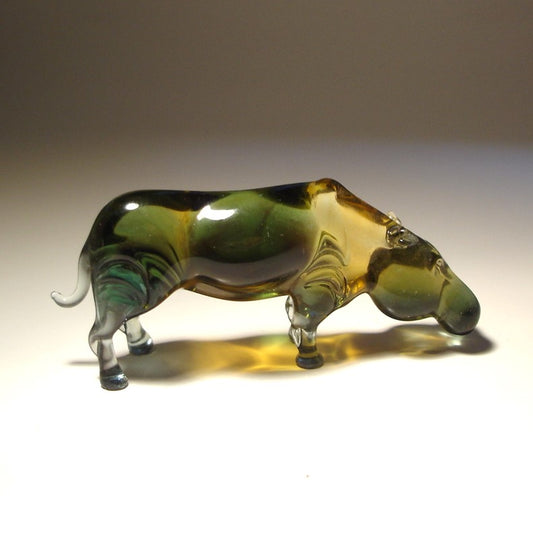 A hand-blown glass hippopotamus figurine with a glossy finish, featuring a color gradient of dark green, amber yellow, and clear glass