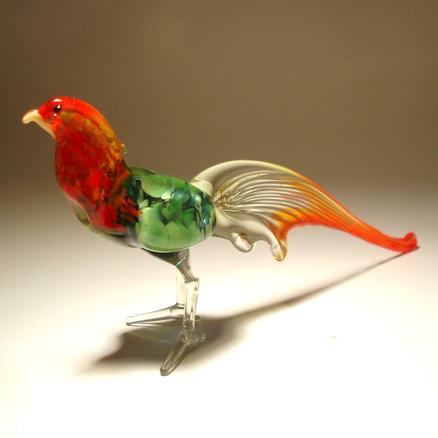 A close-up view of a vibrant glass pheasant figurine, showcasing its green body and red tail.