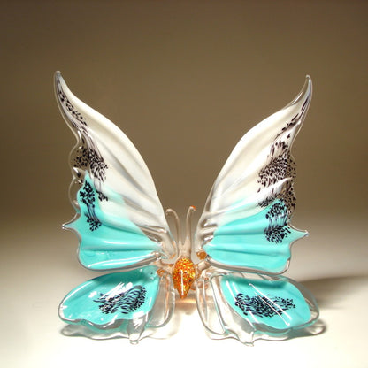 A white and aqua blue  glass butterfly figurine  with red body, sitting.