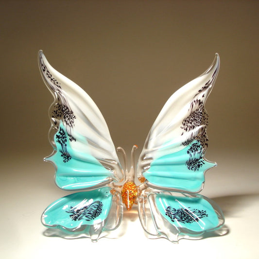 A white and aqua blue  glass butterfly figurine  with red body, sitting.
