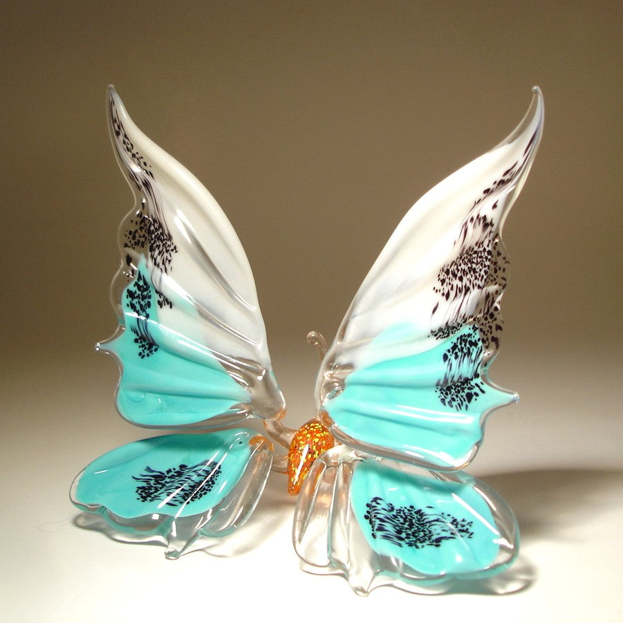 Glass butterfly figurine with WHITE AND turquoise wings and black patterns on a beige background