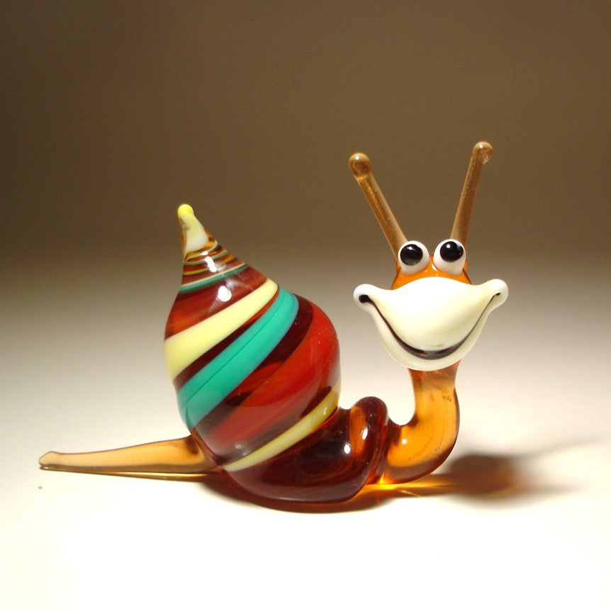 A hand-blown glass snail figurine with a striped shell in red, green, yellow, and brown, and a smiling orange and white face.