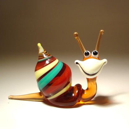 A hand-blown glass snail figurine with a striped shell in red, green, yellow, and brown, and a smiling orange and white face.