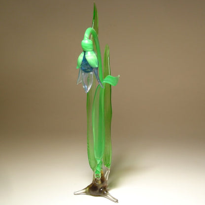 A front view of a delicate glass snowdrop figurine, showcasing its blue petals and slender green stem.