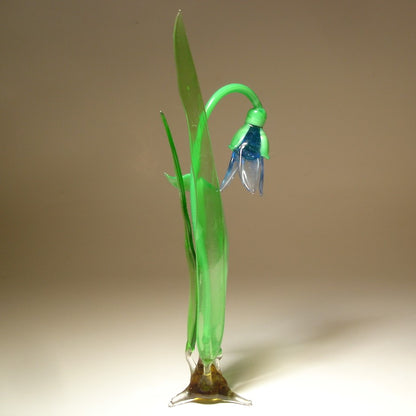 A side view of a glass snowdrop figurine, emphasizing the elegant curves of the petals and the smooth texture of the green stem.