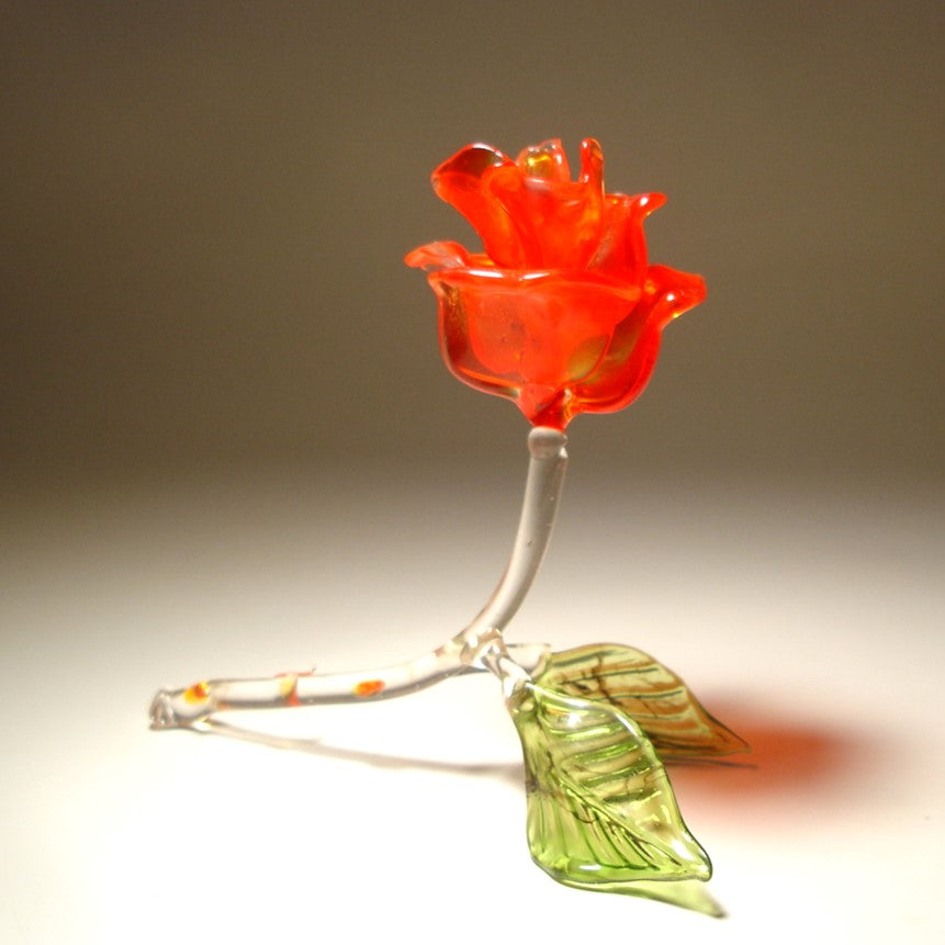 A side view of a red glass rose figurine, showcasing its intricate petals and a stem with red thorns.
