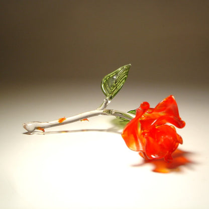 A red rose glass figurine is laying on a side showcasing the details of its beautiful red petals.