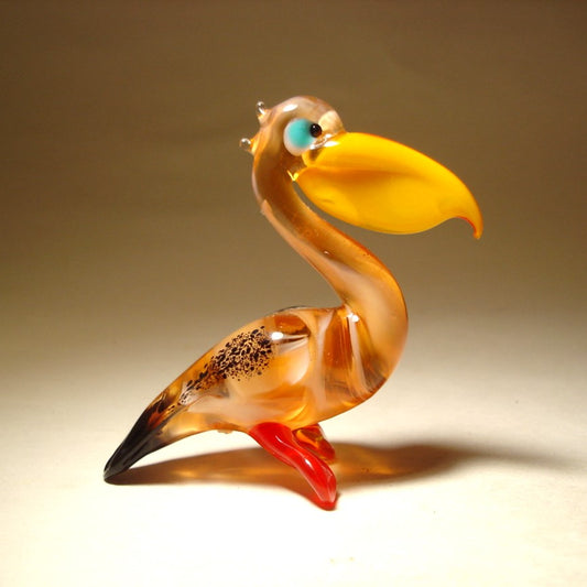 Close-up of a glass pelican figurine featuring a brown and black body, a bright yellow pouch and blue eyes.