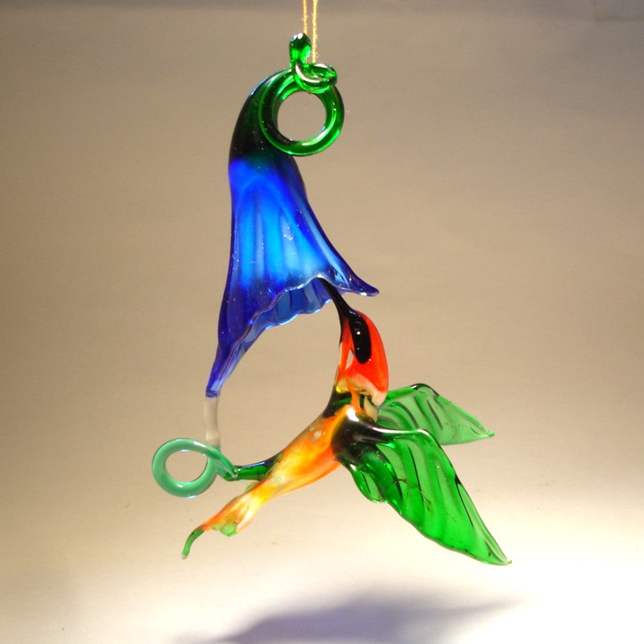 Glass ornament featuring a hummingbird drinking nectar from a blue trumpet flower.