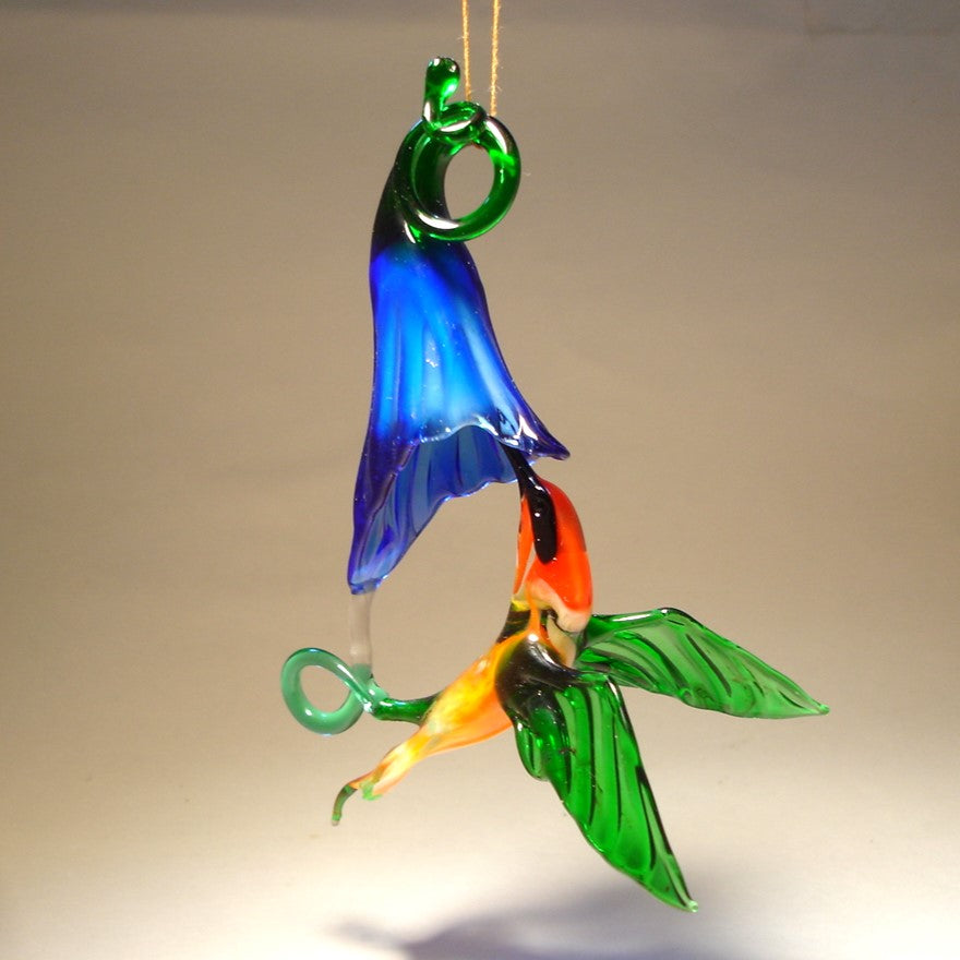 Glass red and green hummingbird figurine hovering next to a vibrant blue flower ornament