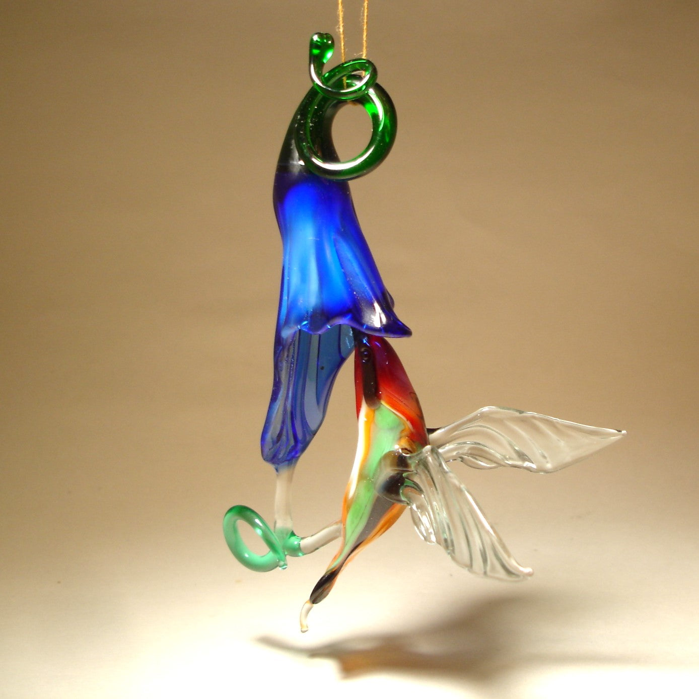 Glass ornament featuring a hummingbird drinking nectar from a blue trumpet flower.