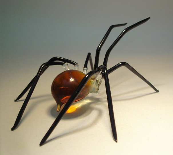 Side view of the handmade glass brown spider figurine, highlighting its shiny, smooth texture and intricate leg design