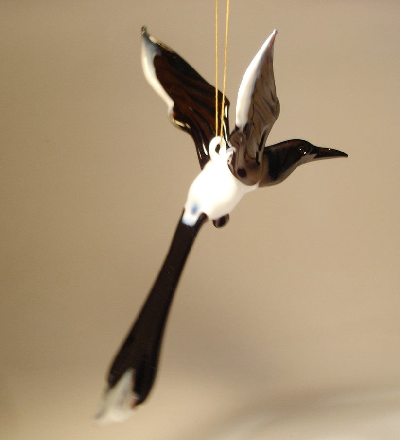 A glass Hanging Bird Magpie figurine ornament, suspended from a thread, showcasing its distinctive black and white feathers 