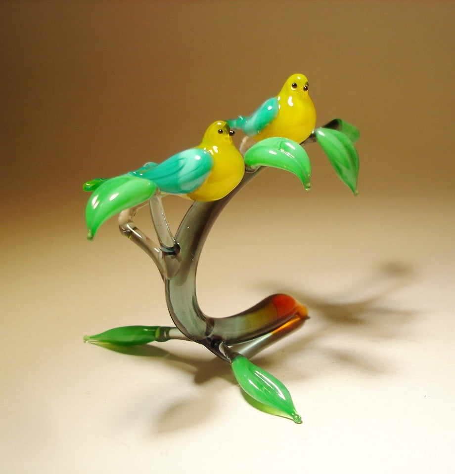 A side profile of the glass yellow birds figurine, showing the birds perched side by side on a curved branch. 