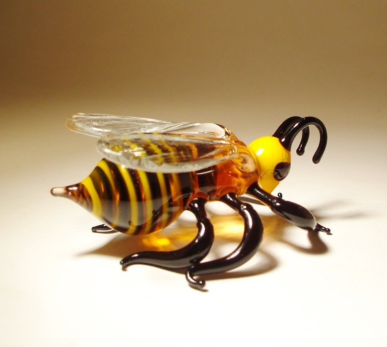 Back view of a glass bee figurine, showcasing its vibrant yellow and black stripes with a pointed stinger.