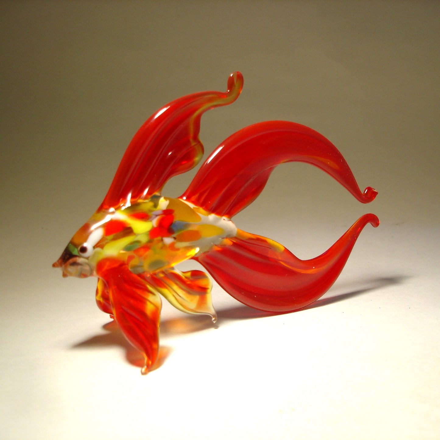 Another side view of a red glass betta fish figurine, showcasing its flowing red fins and vibrant multicolored belly.