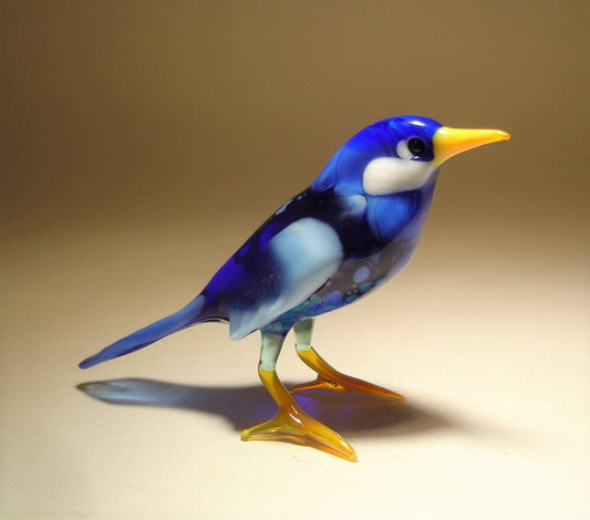 Side view of a glass bluebird figurine, highlighting the detailed wings in lighter blue than the rest of the body and delicate craftsmanship of its head and white cheeks.