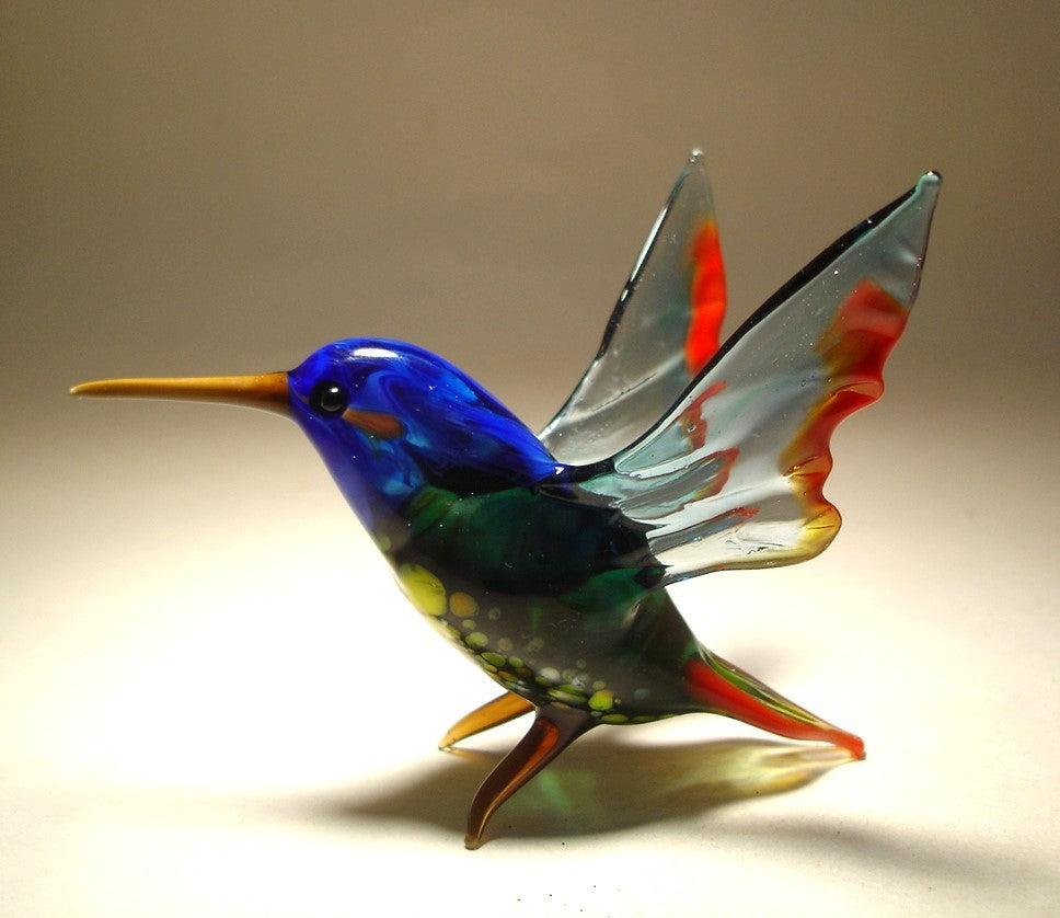 Side view of a glass hummingbird figurine featuring in a sitting pose with its wings outstretched.