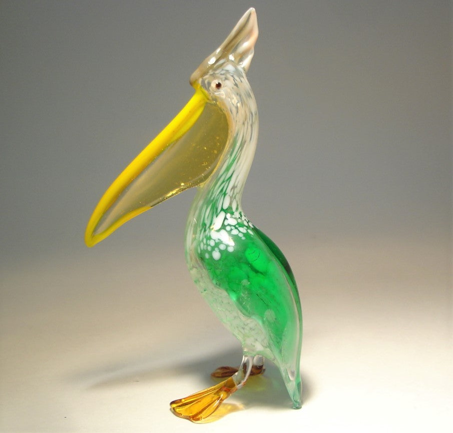 Close-up of a glass pelican figurine featuring a vibrant green body, a bright yellow pouch and white head.