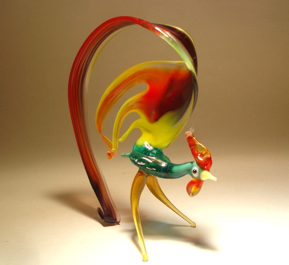 A side view of the glass rooster figurine, highlighting its curved black tail that extends from the body and gently touches the ground, forming the base of support.