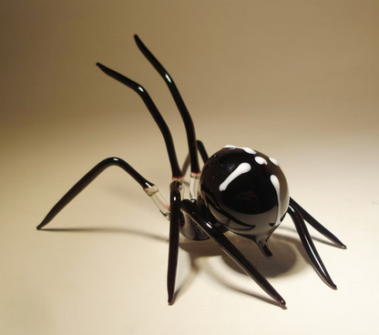 Top view of a handcrafted black glass spider figurine highlighting the white cross on its back 