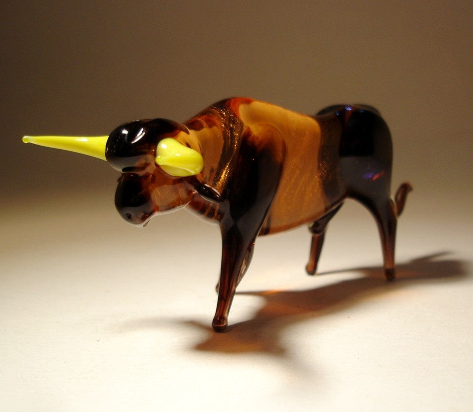 Close-up view of the glass bull figurine, focusing on the sharp, curved yellow horns and detailed facial features.