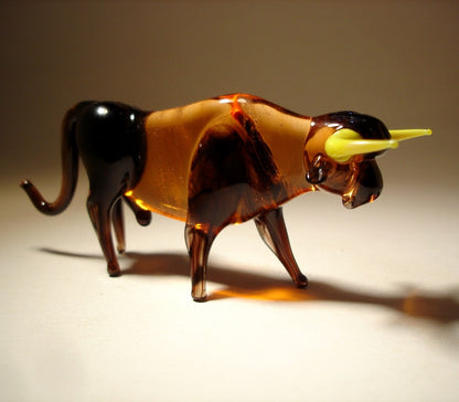 Right side view of a glass bull figurine with yellow horns, showcasing its strong posture and smooth, glossy brown body.