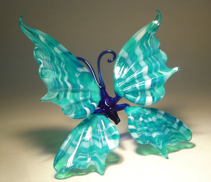 A white and aqua blue striped glass butterfly figurine sitting with its wings.