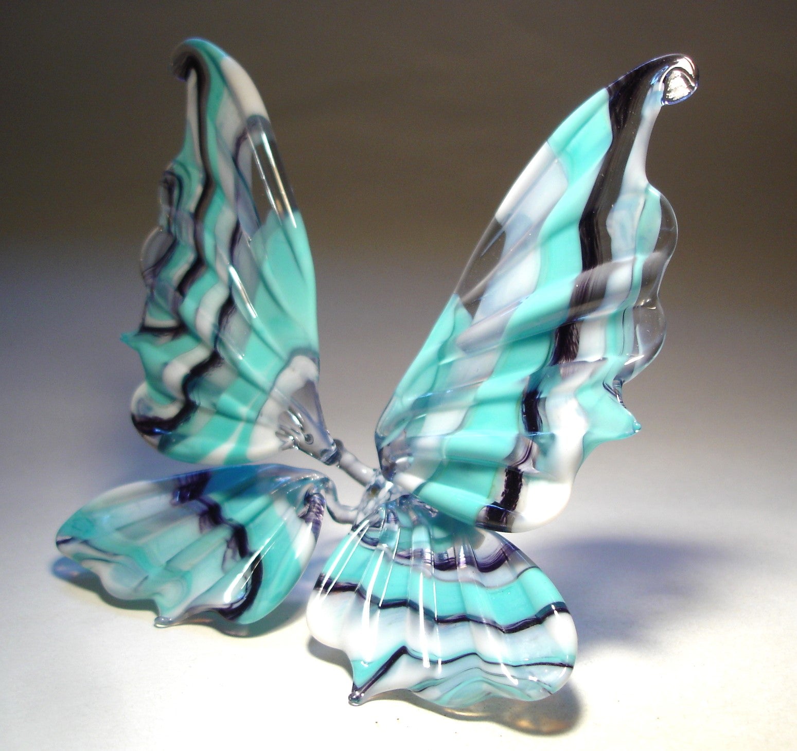 A side view of a white and blue striped glass butterfly figurine, highlighting the elegant curves of its wings and the detailed blue stripes.