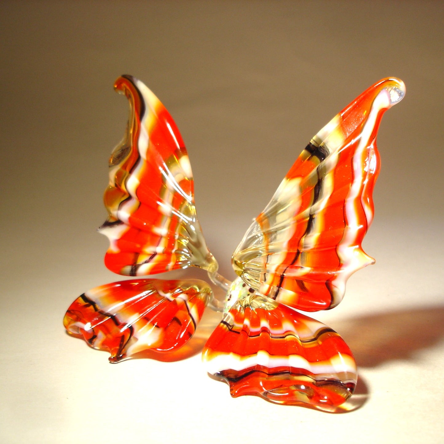 A side view of a red and white striped glass butterfly figurine, highlighting the graceful shape of its wings striped in red, white and black.