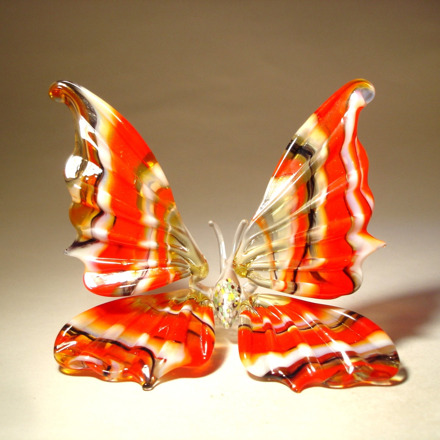 A front view of a handcrafted glass butterfly figurine, showcasing its vibrant colors and intricate striped wing pattern.