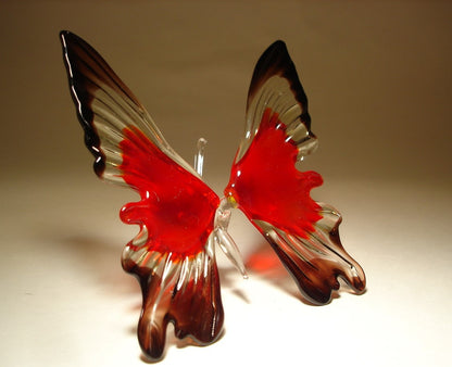 A front view of a red and black glass butterfly ornament, showcasing its intricate wing patterns and vibrant colors, with clear glass antennae.