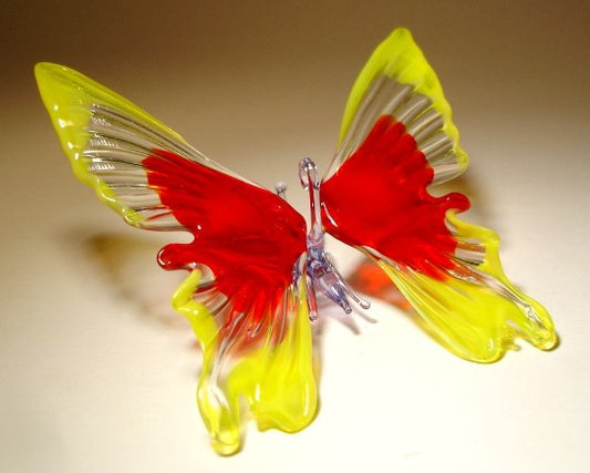 Close-up of a yellow and red glass butterfly ornament, showcasing its vibrant open wings and intricate detailing. 