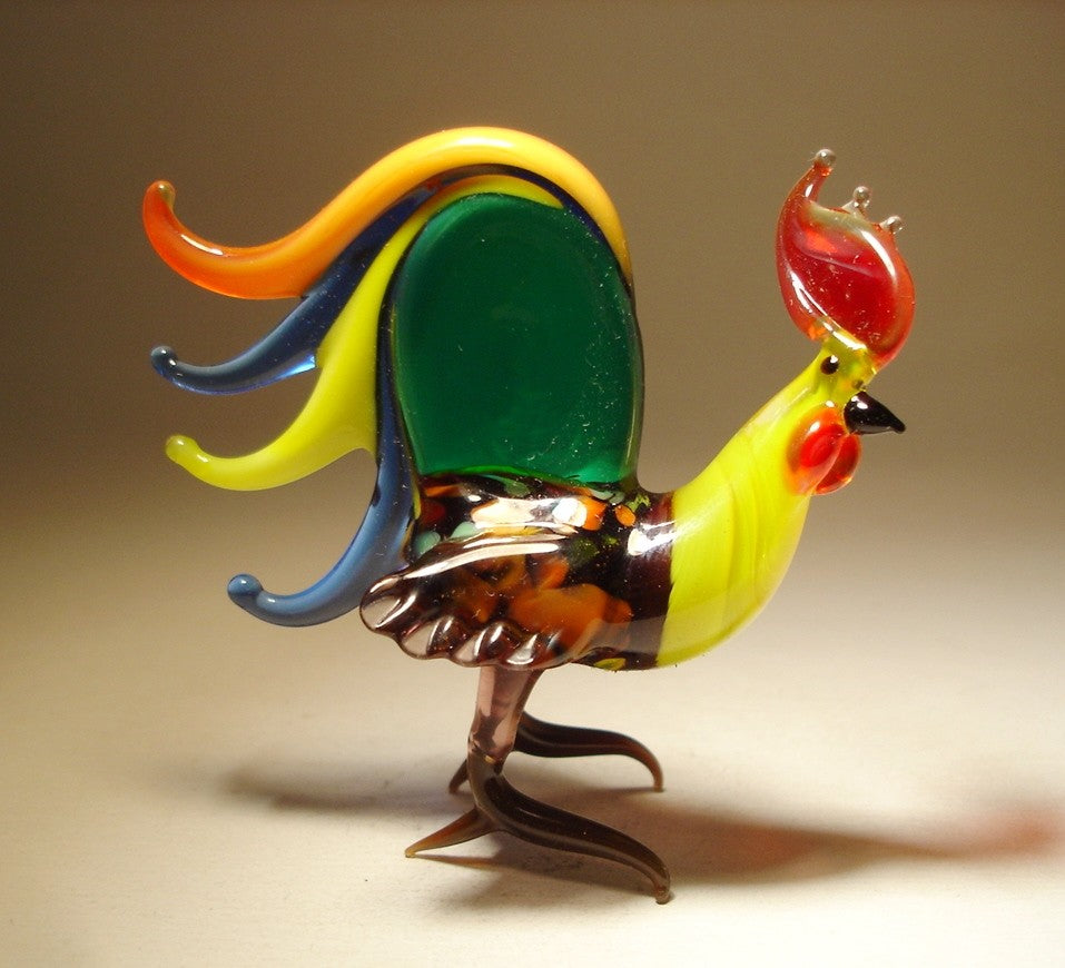 A side view of a glass rooster figurine, highlighting its impressive, colorful tail feathers that fan out elegantly