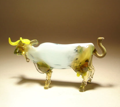 Side view of the glass cow figurine, showcasing its detailed legs, curled up tail, and white body.