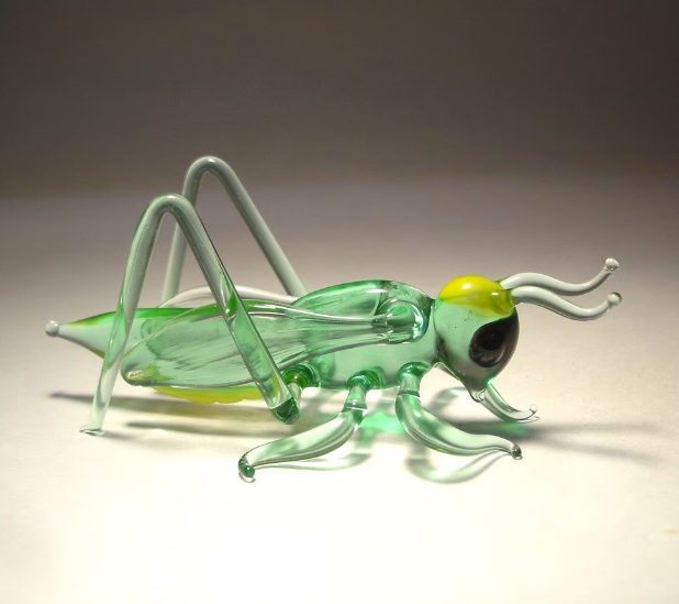 Side view of the glass cricket grasshopper figurine, showcasing the craftsmanship in the body and finely sculpted antennae.