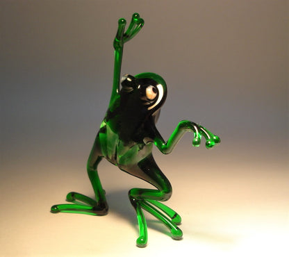 Black view of a glass frog figurine in a dancing pose, with one leg slightly lifted and arms gracefully extended.