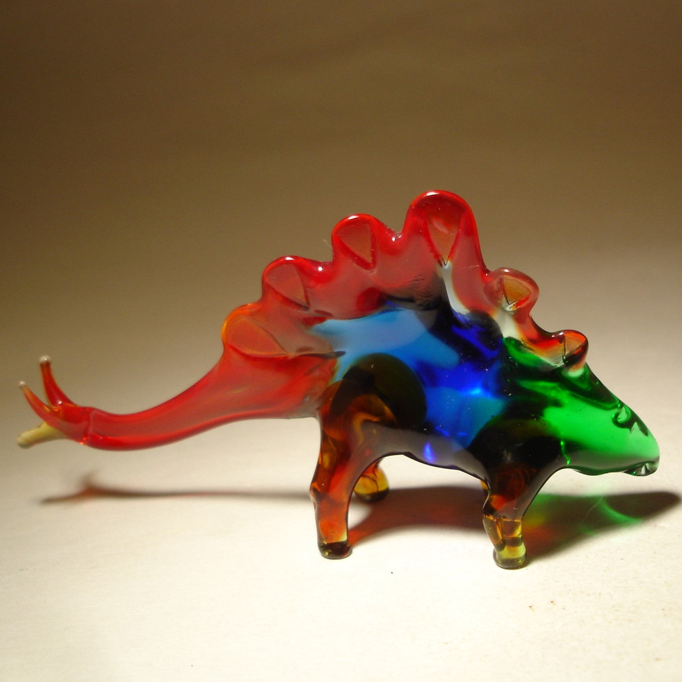 A handmade blown glass figurine of a Stegosaurus, featuring a vibrant, smooth body with delicate details.