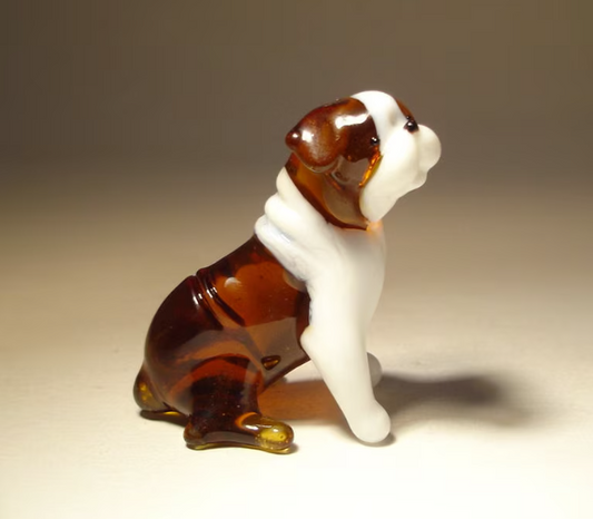 A detailed glass figurine of a sitting English Bulldog with a glossy finish in shades of brown and white.