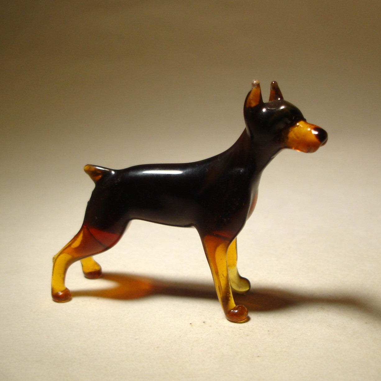 Handcrafted glass Doberman figurine standing tall with a sleek black body and brown markings.