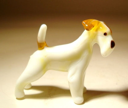 A glass Fox Terrier dog figurine standing upright showcasing its distinctive wiry coat  and upward tail.