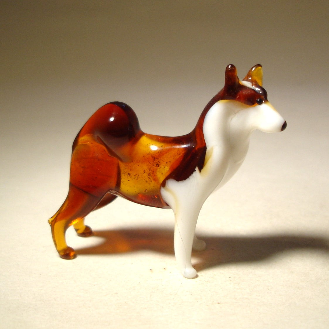 The glass Siberian Husky figurine is shown from a side angle, highlighting its muscular build and bushy tail curled over its back.