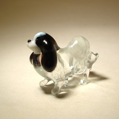 The glass Japanese Chin figurine from a side angle, emphasizing its graceful posture and the beautiful, contrasting black and colors of its coat.