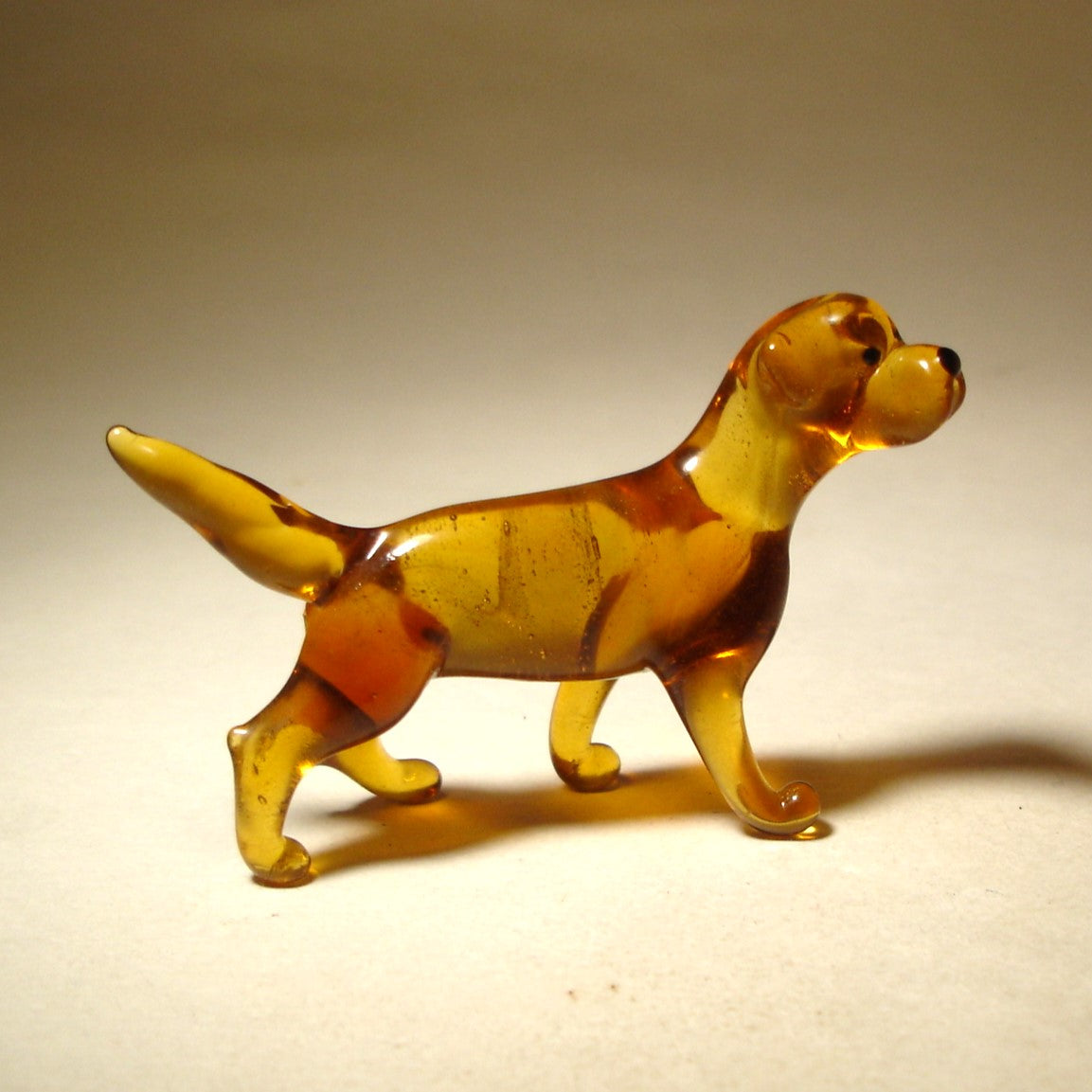 Aglass Yellow Lab figurine is shown from the side, showcasing its sturdy build, strong legs, and wagging tail.