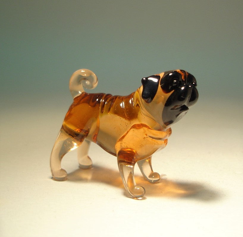 A fawn glass Pug figurine in a playful pose, featuring its signature wrinkled face and curled tail.